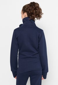 Námořnická fleecová bunda s vysokým límcem, dlouhými rukávy a texturovaným povrchem. Elegantní, přiléhavý design vhodný pro volnočasové nošení.