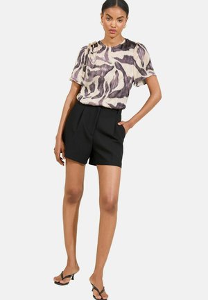 Top à manches courtes avec un motif abstrait violet et crème et des détails aux épaules, associé à un short noir taille haute.