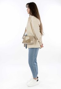 Beige kordflamsjacka, blå denimjeans och vita sneakers. En beige axelremsväska har en geometrisk patchwork-design.