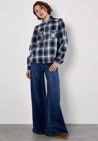 Blue plaid flannel shirt with two chest pockets, paired with wide-leg denim jeans. Both garments exhibit a relaxed fit and casual style.