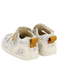 Zapatos infantiles blancos con patrones de dinosaurios azules, parte superior texturizada y una correa beige. Presenta una puntera redondeada y un collar acolchado.