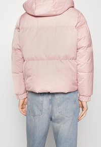 Ljusrosa vadderad jacka med huva, som har en jämn textur, elastiska ärmar och en kort längd, kombinerad med ljusblå jeans.