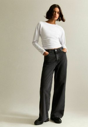 Biała bluzka z długim rękawem w połączeniu z czarnymi, luźnymi dżinsami z wysokim stanem oraz masywnymi czarnymi butami. Prosty wzór, miękka faktura oraz schludne linie.