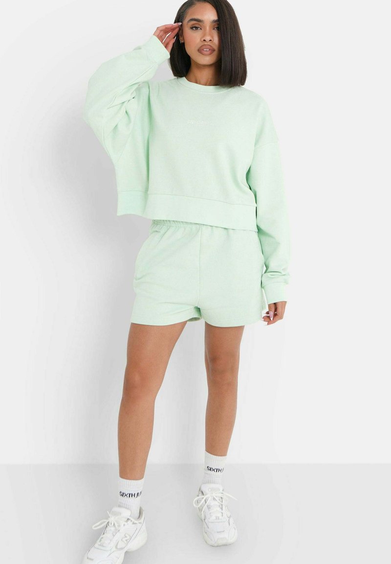 Lichtgroene cropped sweatshirt met lange mouwen, gecombineerd met bijpassende shorts. Zachte textuur, elastische tailleband op de shorts en zichtbare stiksels.