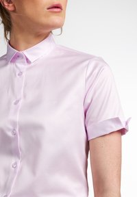 Blusa in satin rosa con colletto a punta, maniche corte arrotolate e chiusura frontale con bottoni. Texture liscia con un leggero lucido.