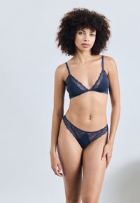 Tumes navy aluspesu komplekt, mis sisaldab pitsäärisega bralette'i õhukeste rihmadega ja sobiva stringi. Pehme, elastne kangas pitsdetailidega.