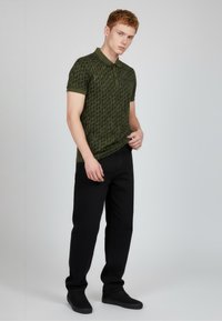 Polokošile tmavě zelená s jemným vzorem, krátkými rukávy a límečkem, doplněná černými kalhotami a černými teniskami.