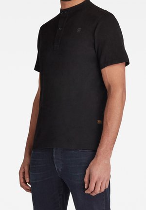 Schwarzes Poloshirt mit kurzen Ärmeln und Stehkragen, Zwei-Knopf-Leiste und dezentem Logo auf der Brust; glatte Stoffstruktur.