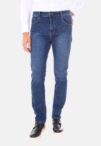 Jeans in denim di colore blu scuro con una vestibilità slim. Presentano cinque tasche, dettagli di cucitura e chiusura con bottone. Abbinati a scarpe nere.