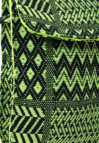 Tessuto nero e verde neon con motivi geometrici, caratterizzato da zigzag e diamanti, contornato da cuciture gialle brillanti.