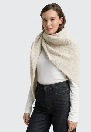 Écharpe enveloppante texturée beige en matériau doux, drapée autour des épaules. Elle présente une surface duveteuse avec des bords effilochés.