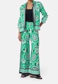 Ensemble chemise à imprimé floral vert et blanc et pantalon à jambes larges, confectionné en tissu léger, avec des accents contrastants noirs et des détails à boutons.