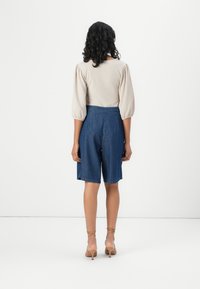 Blusa texturizada de bege claro com mangas bufantes, combinada com calções de ganga azul escuro, até à altura da coxa, design casual e detalhes de costura nas costas.