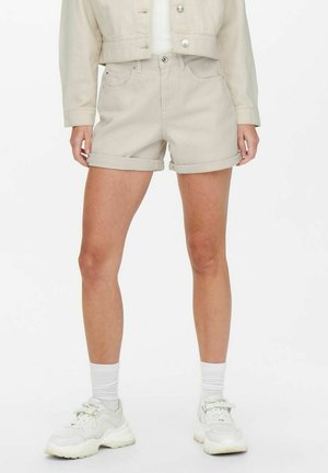 Beiga denimshorts med uppvikt fåll, som har två framfickor och en knappstängning, ihopparat med vita sneakers och strumpor.