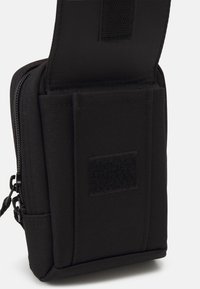 Saco de tecido preto com fecho de correr, orientação vertical, superfície texturizada, etiqueta de Velcro e costura reforçada nas bordas.