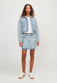 Giacca di denim azzurro chiaro con chiusura a bottoni e design corto, abbinata a una gonna di denim coordinata con tasche laterali e una leggera sfumatura.