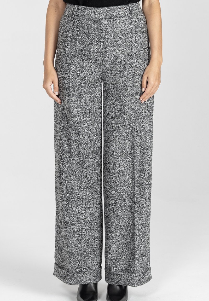 Szerokie spodnie w teksturowanym czarno-białym dzianinie, z wysokim stanem i mankietami, w połączeniu z czarnym obuwiem.