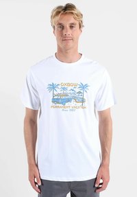T-shirt en coton blanc avec une impression graphique de palmiers et d'une camionnette, avec les textes "OXBOW" et "PERMANENT VACATION" en bleu et or.