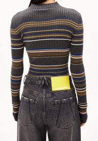 Top à manches longues côtelé gris avec des rayures multicolores ; associé à un jean noir taille haute avec des poches arrière et une étiquette de marque jaune.
