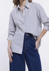 Jasnoniebieska koszula w poziome białe paski, zapinana na guziki, z kieszonką na piersi, kołnierzykowa, z długim rękawem. Połączona z ciemnoniebieskimi, wysokimi dżinsami.