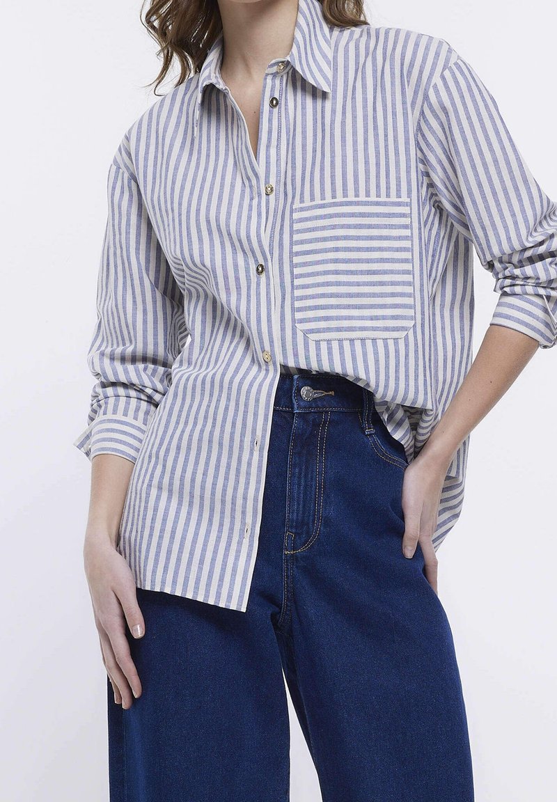 Jasnoniebieska koszula w poziome białe paski, zapinana na guziki, z kieszonką na piersi, kołnierzykowa, z długim rękawem. Połączona z ciemnoniebieskimi, wysokimi dżinsami.