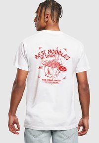 T-shirt blanc avec une impression graphique rouge d'une boîte à emporter de nouilles, des baguettes et le texte "LES MEILLEURES NOUILLES DE LA VILLE." Comprend des coordonnées.