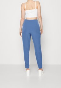 Blå tapered byxor i ett mjukt tyg med hög midja. Har en ren design och en bekväm passform, tillsammans med vita klackskor.