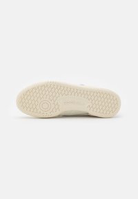 Béžová podrážka tenisky s texturovaným gumovým povrchem a diamantovým vzorem, s vyraženým logem "Reebok" pro branding.