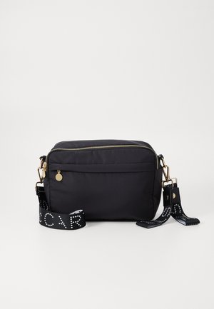 Bolsa de ombro em tecido preto com ferragens douradas, fecho com zip e alça ajustável, apresentando um padrão de bolinhas brancas. Textura suave, forma retangular.