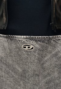 Γκρι τζιν με όξινο πλύσιμο και μικρό οβάλ κεντημένο λογότυπο πάνω από την τσέπη, φορεμένο με μαύρο μπλουζάκι με ριμπ ύφανση και μαύρο δερμάτινο μπουφάν με φερμουάρ.