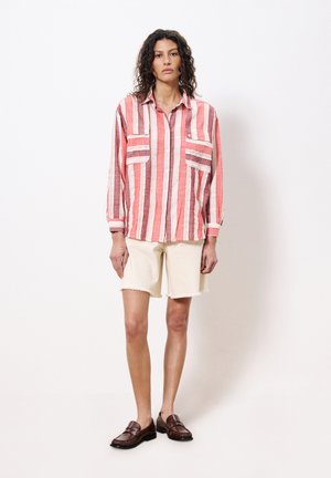 Rood-wit gestreepte langoeve shirt met twee borstzakken, gecombineerd met crèmekleurige shorts en bruine instappers, staand tegen een witte achtergrond.