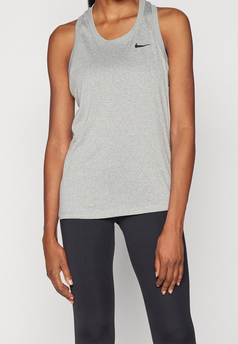 Femme portant un débardeur gris Nike sans manches et un legging noir, debout, les bras détendus le long du corps.