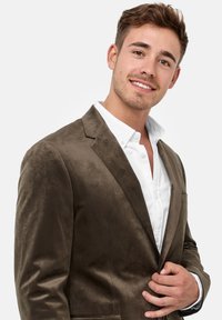 Brun semsket blazer med en jevn tekstur, enkel knappelukking og klaftelapper, parret med en hvit skjorte.