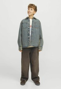 Jeansjacka med två bröstfickor, ljusblå tvätt, avslappnad passform, knäppning med knappar. Kombinerad med oversized bruna byxor och mörka skor.