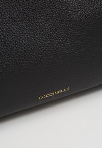 Sort struktureret læder handbag med et gold "Coccinelle" logo. Tasken har en glat finish med en kornet overflademønster.