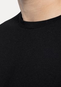 Camiseta de algodón negra con cuello redondo. La textura parece suave y ligeramente peluda, sin logotipos ni patrones visibles.