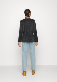 Top glitterato nero con maniche lunghe e vita peplum, abbinato a jeans dritti azzurri e scarpe con tacco a blocco marroni.