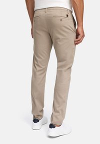 Beige katoenen broeken met een slim fit, twee achterzakken en een bruin leren logopatch, gecombineerd met witte sneakers.