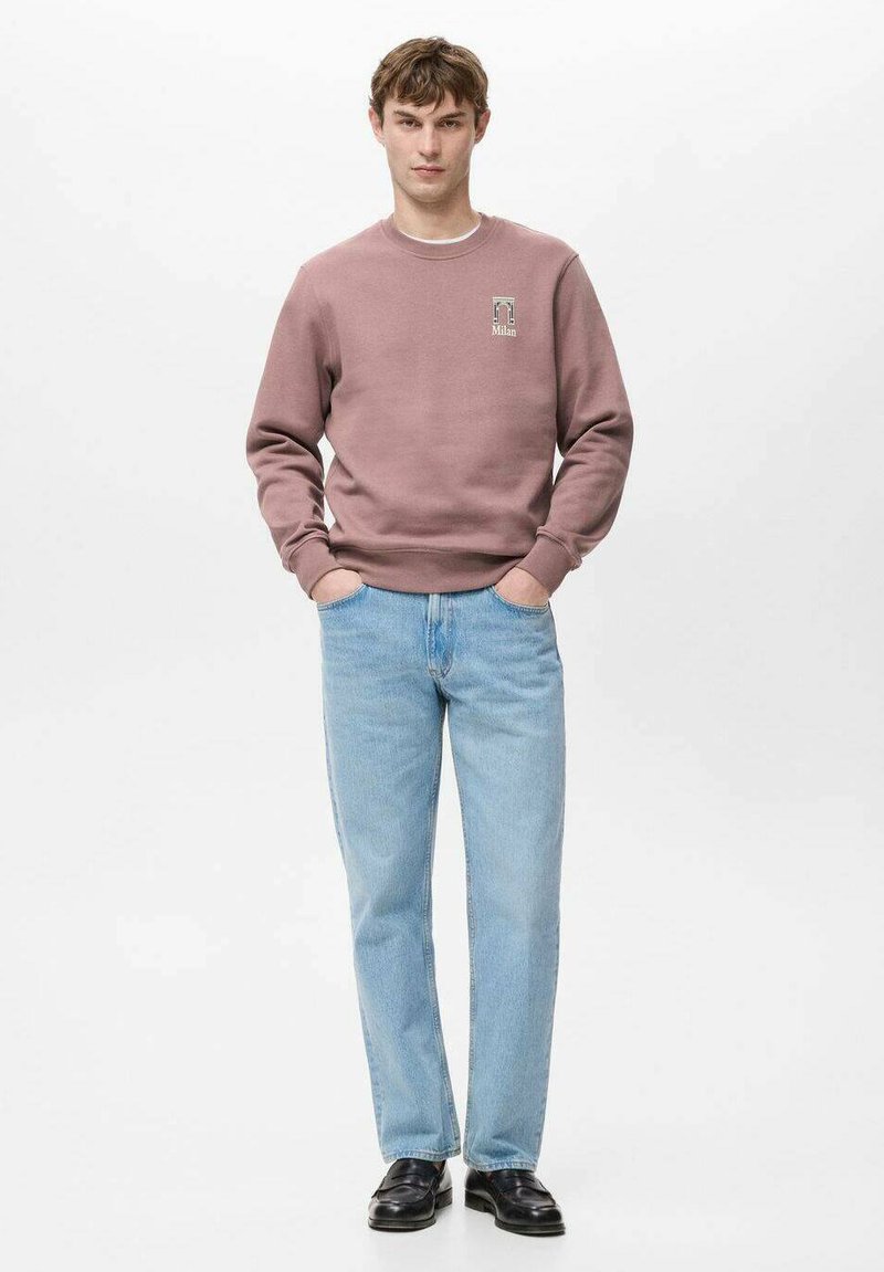 Pullover-Sweatshirt in staubigem Rosa, mit kleinem Motiv auf der Brust. Kombiniert mit hellblauen Jeans und schwarzen Schuhen. Einfacher, lässiger Look.