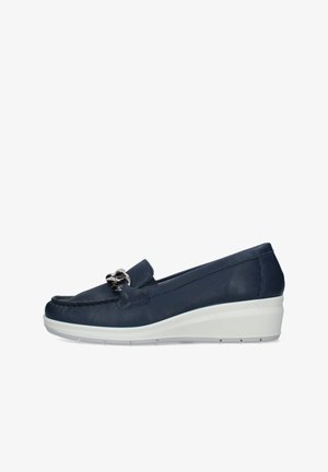 Mocassino con zeppa blu navy con suola bianca e dettaglio catena argento sulla parte superiore, inclinato a sinistra su sfondo bianco.