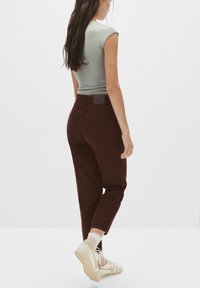 Jeans burgundy cu talie înaltă și picior tapered, cu buzunare la spate și un material texturat. Asortați cu adidași bej și șosete albe.