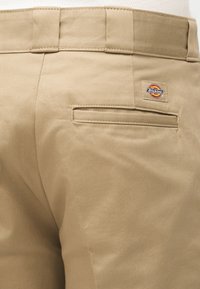 Οπίσθια όψη μπεζ παντελονιών Dickies που δείχνει το κεντημένο πίσω τσέπη και την ετικέτα της μάρκας πάνω από την τσέπη.