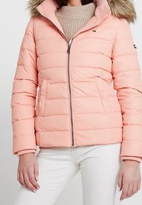 Różowa ocieplana kurtka z kapturem obszytym futerkiem, zamkiem błyskawicznym z przodu i ściągaczami na rękawach. Posiada pikowany wzór oraz logo na rękawie.