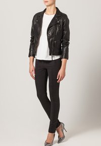 Giacca da motociclista in pelle nera con tasche con zip, t-shirt bianca e pantaloni neri con texture. Completato con tacchi alti argentati.