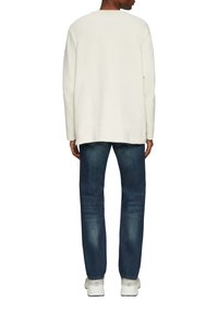 Lange mouwen crèmekleurig shirt, ontspannen pasvorm, gecombineerd met donkerblauwe spijkerbroek en witte sneakers. Katoenen textuur met minimale naden.