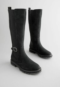 Black knee-high boots with a textured upper, interior zip, strap accent, and rugged rubber soles for traction. Smooth finish on the front.