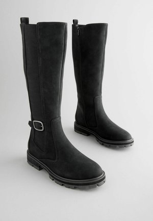 Svarta knähöga stövlar med en strukturerad ovansida, inre dragkedja, bandleverans och slitstarka gummisulor för bra grepp. Slät yta fram.