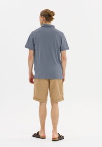 Ljusblå pikétröja med korta ärmar, kombinerad med beige shorts med upprullade fållar och mörka slidesandaler. Diskret textur, avslappnad design.