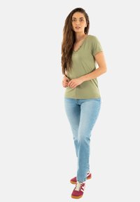 T-shirt vert olive à manches courtes et col en V associé à un jean bleu et des baskets rouges avec des accents blancs et des semelles marron clair.