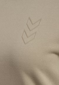 Deux formes chevron beiges imprimées sur un tissu texturé marron clair, probablement une partie d'un vêtement.
